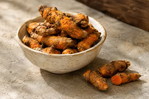 Morceaux orange de racine de curcuma séchée dans une coupelle en céramique sur pierre claire.