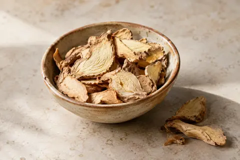 Morceaux de racine de gingembre séchée présentés dans une céramique artisanale sur pierre claire.