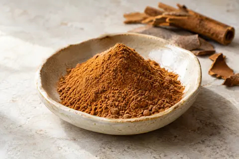 Cannelle de Ceylan en poudre brun cuivré présentée dans une coupelle artisanale sur pierre claire.