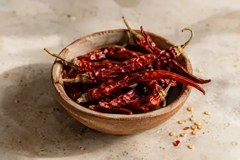 Piments de Cayenne entiers séchés disposés dans une céramique artisanale sur une pierre claire.