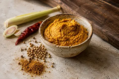 Pâte de curry jaune dans une coupelle en céramique, entourée de piment et d’aromates