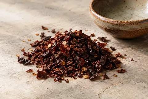 Flocons de chipotle fumé rouge sombre disposés sur une pierre claire près d’une céramique