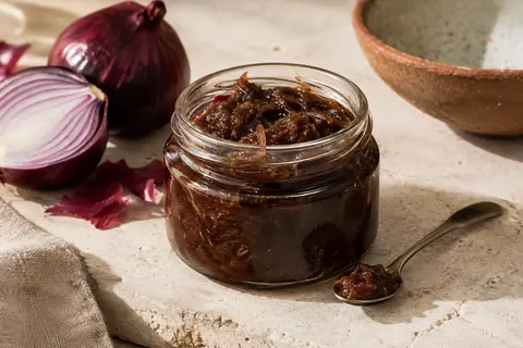 Bocal en verre de chutney d’oignon rouge de Tropea, brun chocolat et tartinable, posé sur une pierre claire.