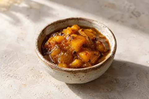 Chutney à la mangue épicée servi dans une petite céramique artisanale sur une pierre claire.
