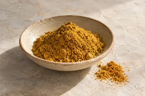 Mélange de ras el hanout jaune en poudre présenté sur une céramique artisanale claire, avec ses nuances dorées.