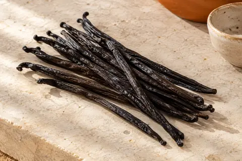 Dix gousses de vanille Bourbon sombres et souples disposées sur une pierre claire.