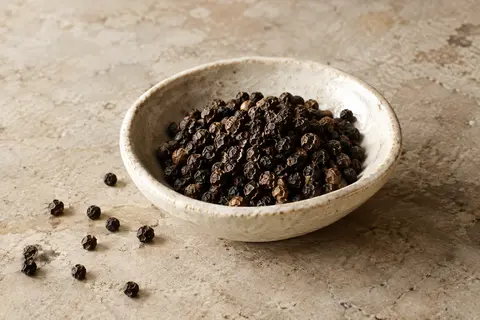 Grains de poivre noir de Kampot dans une coupelle en céramique sur une pierre claire