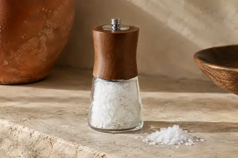 Moulin de table rechargeable Maldon contenant des flocons de sel de mer, posé sur une pierre claire.