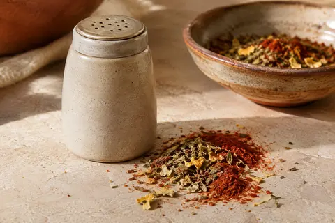 Mélange d’épices Arizona Chicken dans une saupoudreuse, présenté avec une petite portion de poudre sur une pierre claire.