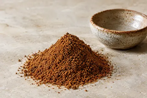 Poudre Baharat brun chaud présentée sur une pierre claire près d’une coupelle en céramique