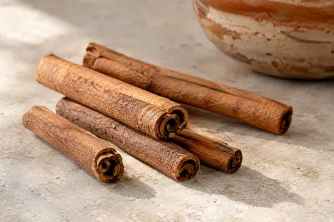 Bâtons de cannelle entiers bruns disposés sur une pierre claire dans une lumière naturelle douce