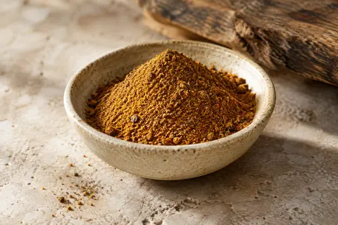 Poudre de ras-el-hanout aux tons chauds présentée dans une coupelle en céramique sur une pierre claire.