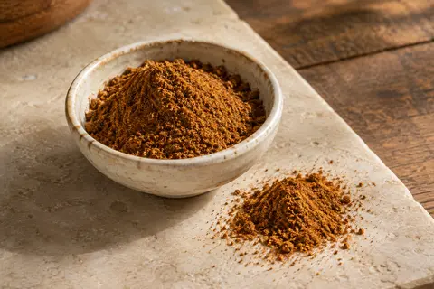 Ras el hanout en poudre dans une coupelle en céramique posée sur une pierre claire