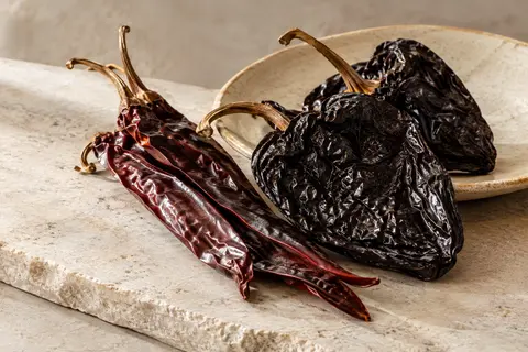 Piments séchés entiers Guajillo et Ancho réunis sur une céramique claire.