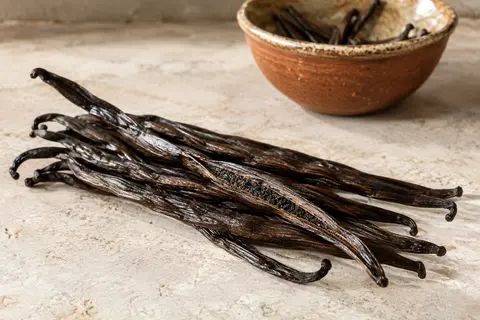 Gousses entières de vanille Bourbon de Madagascar, sombres et charnues, disposées sur une pierre claire.